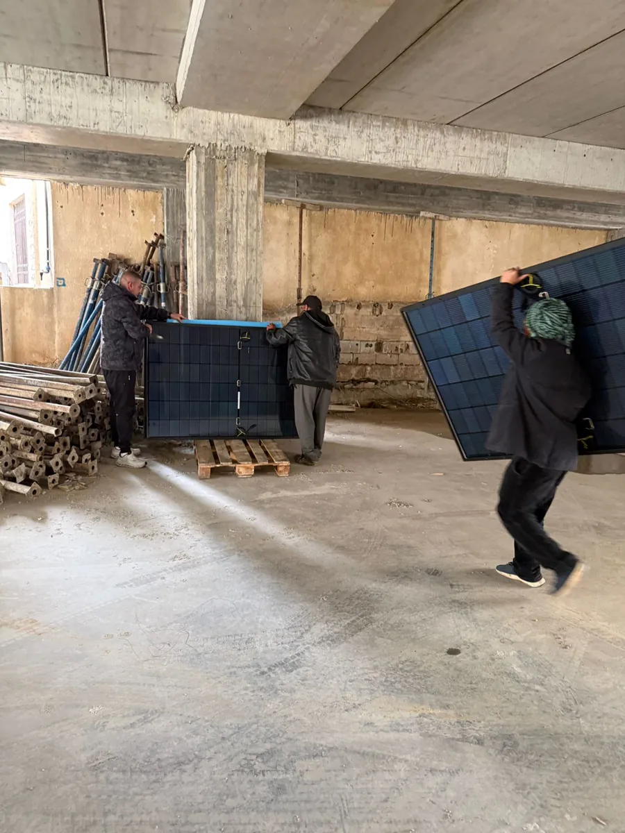 Helfer tragen Solarmodule in einen Rohbau im Libanon